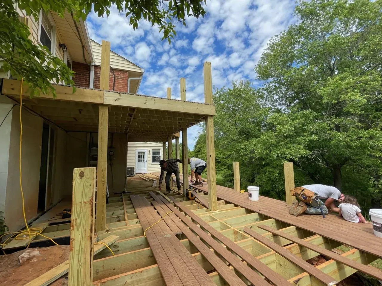 A group of people are working on a wooden deck in front of a house.