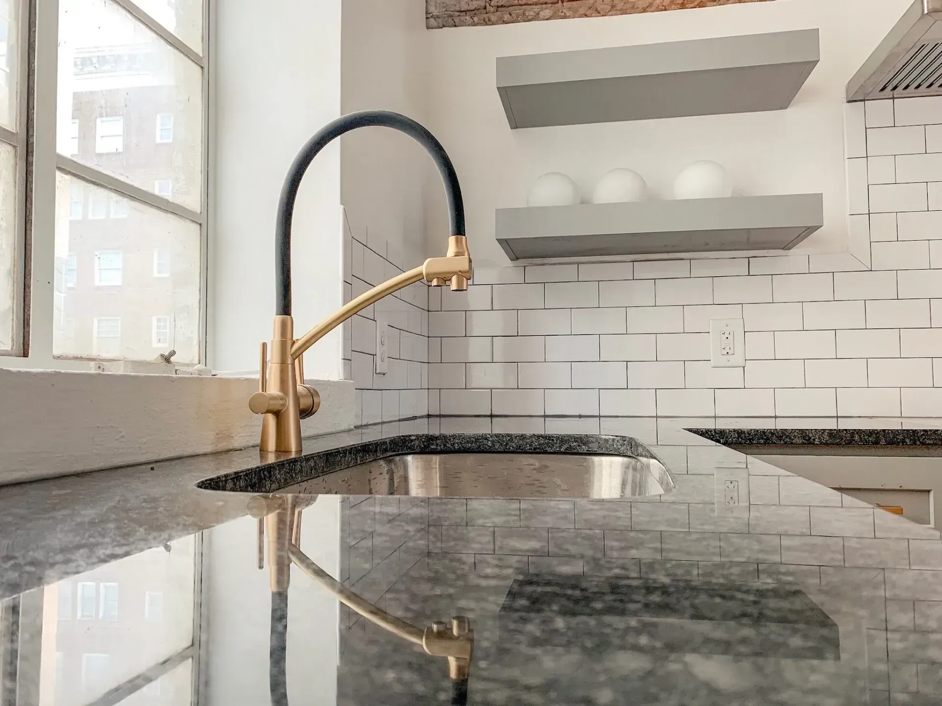 A kitchen with a sink , faucet , and shelves.