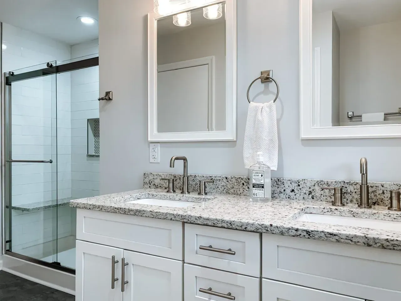 A bathroom with two sinks , two mirrors and a walk in shower.