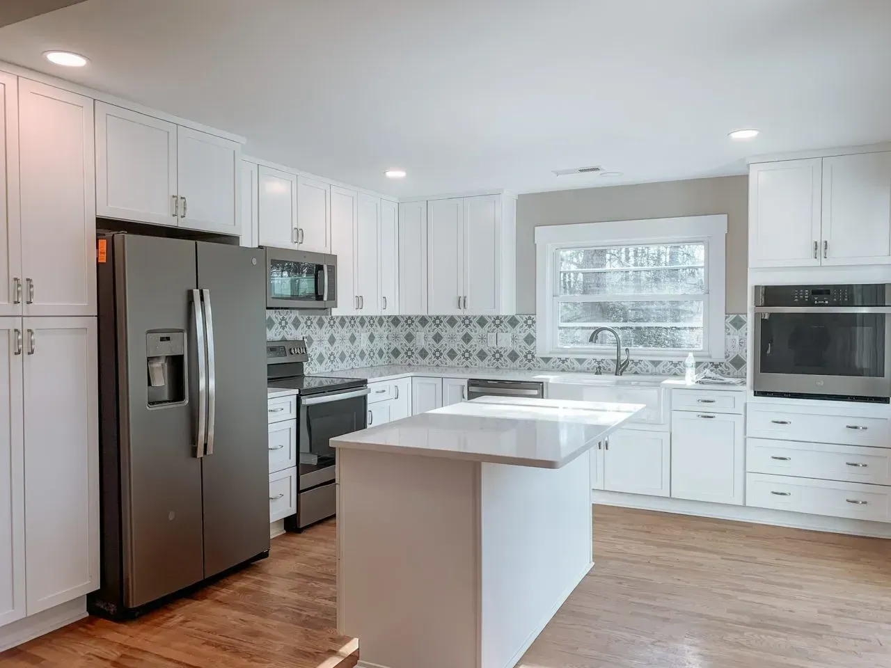 A kitchen with white cabinets , stainless steel appliances and a large island.