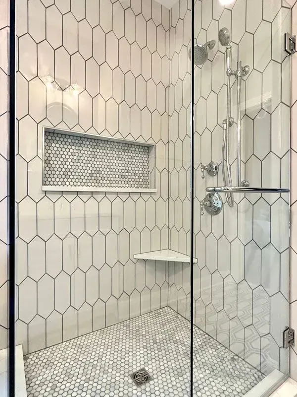 A shower with white tiles and a glass door.