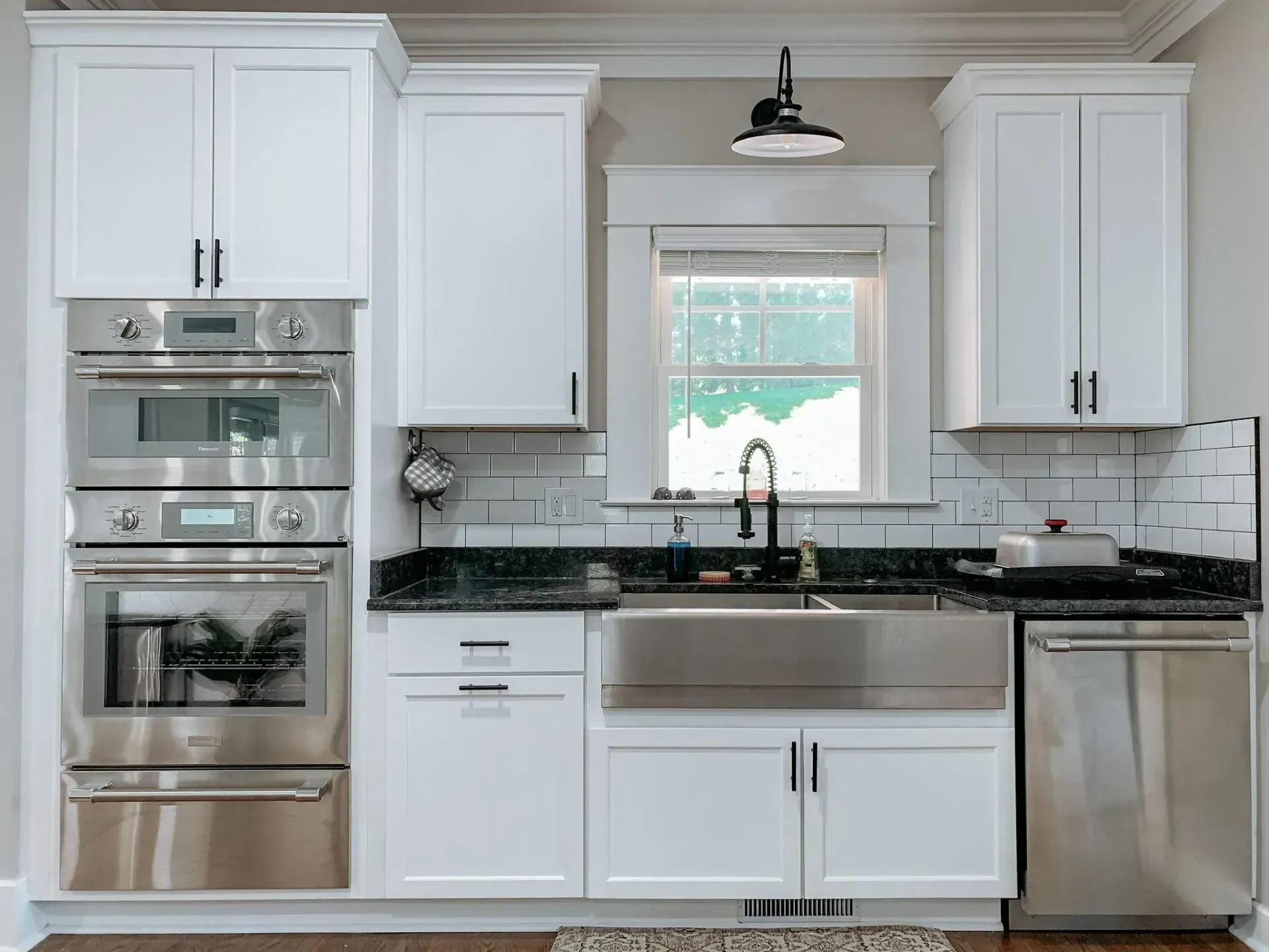 A kitchen with white cabinets , stainless steel appliances , a sink , and a window.