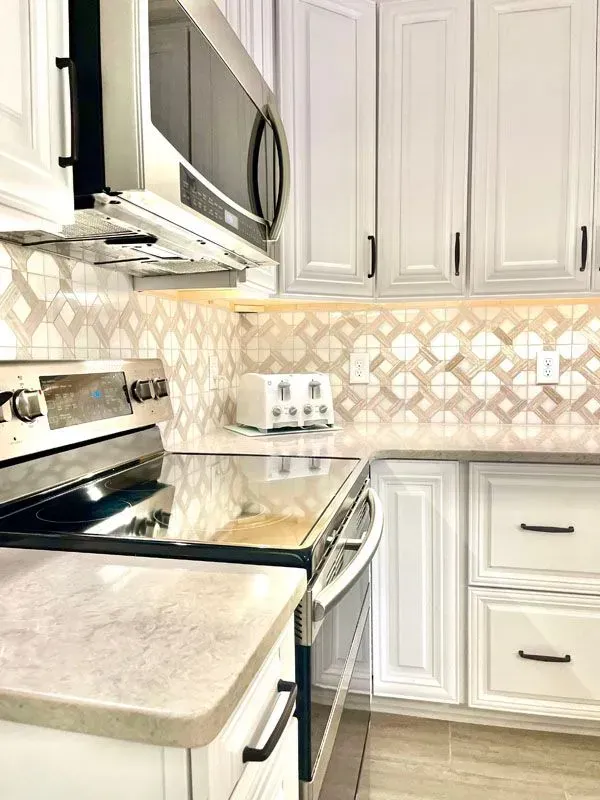 A kitchen with white cabinets , a stove , a microwave , and a toaster oven.