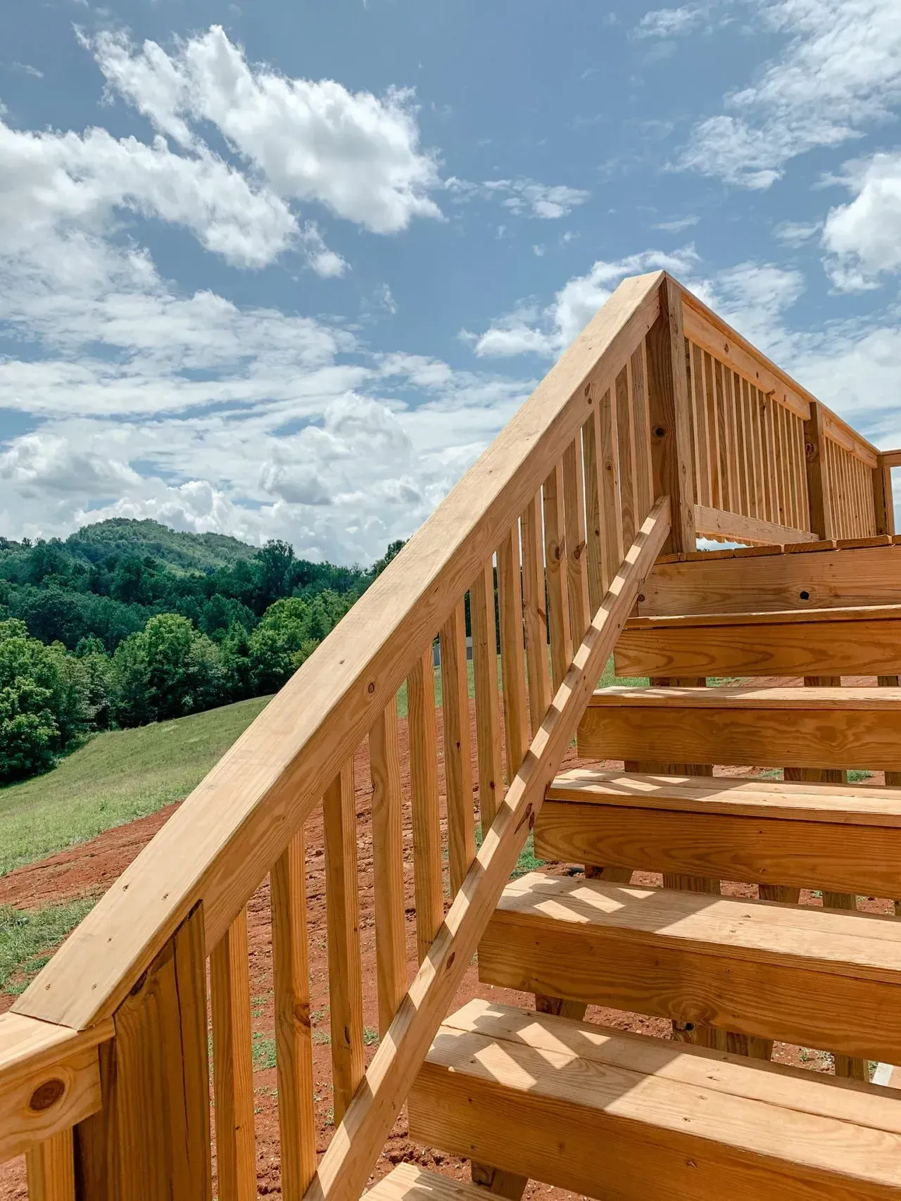 A wooden deck with stairs leading up to a view of a field and mountains.