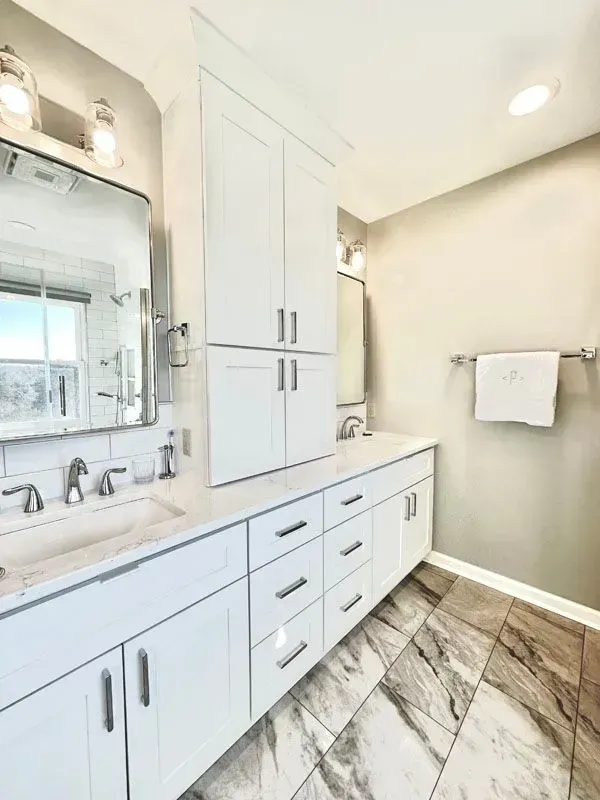 A bathroom with two sinks , a mirror , and white cabinets.