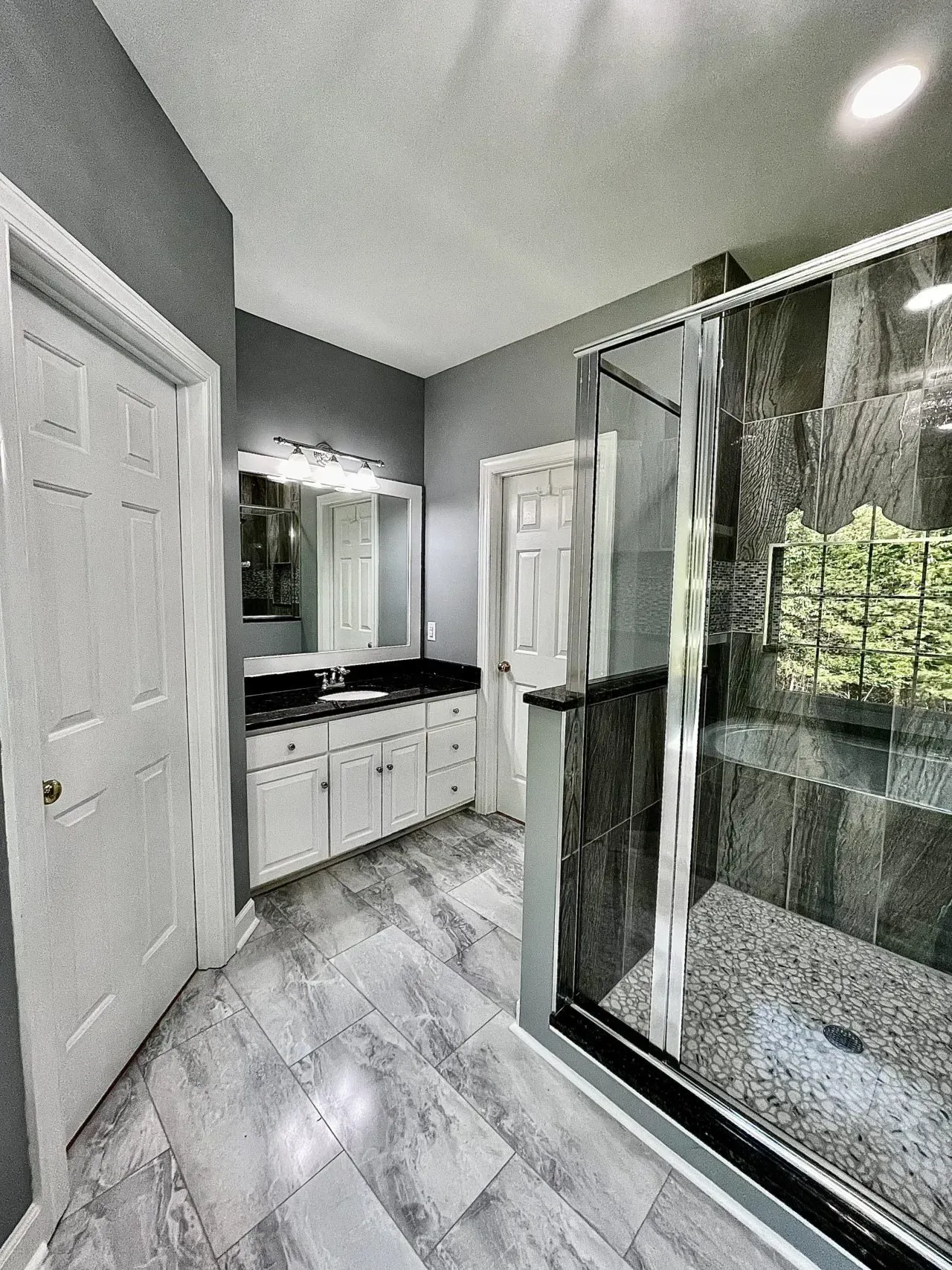 A bathroom with a walk in shower , sink and mirror.