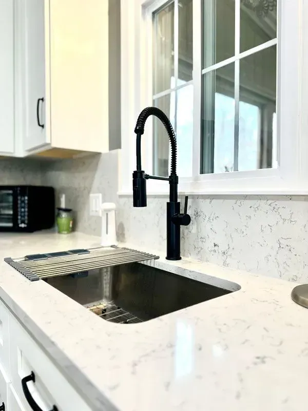 A kitchen sink with a black faucet and a window