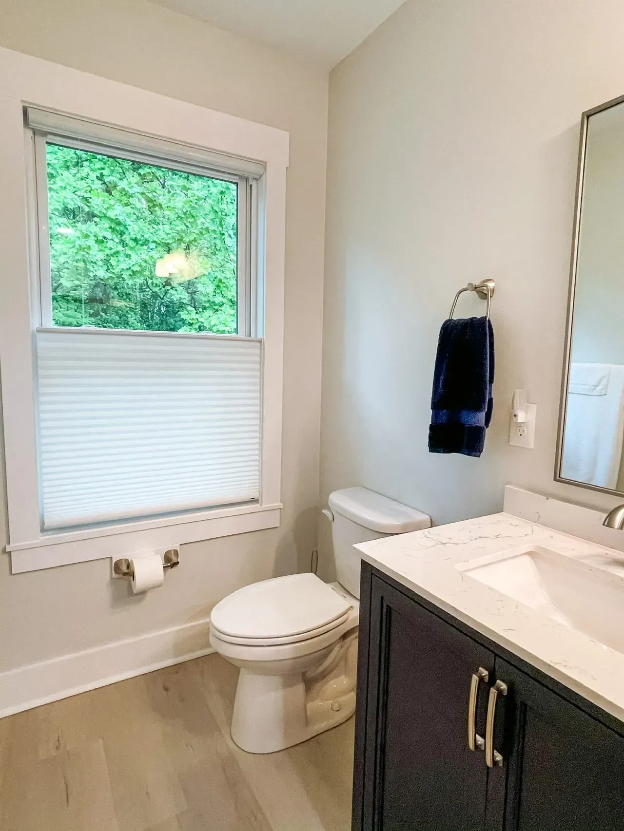 A bathroom with a toilet , sink , mirror and window.