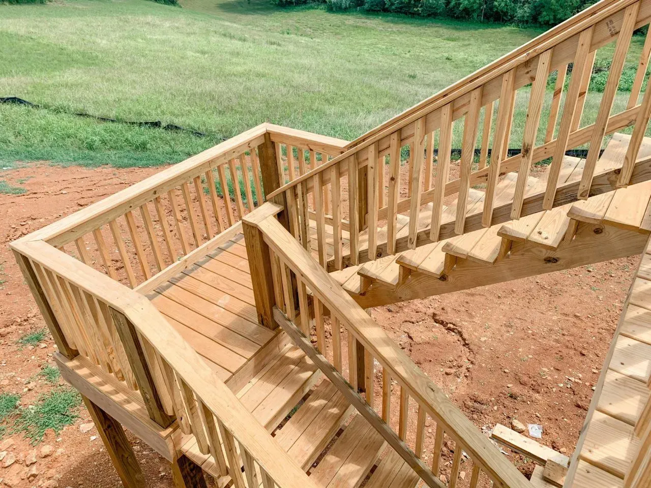 A wooden deck with stairs leading up to a grassy field.