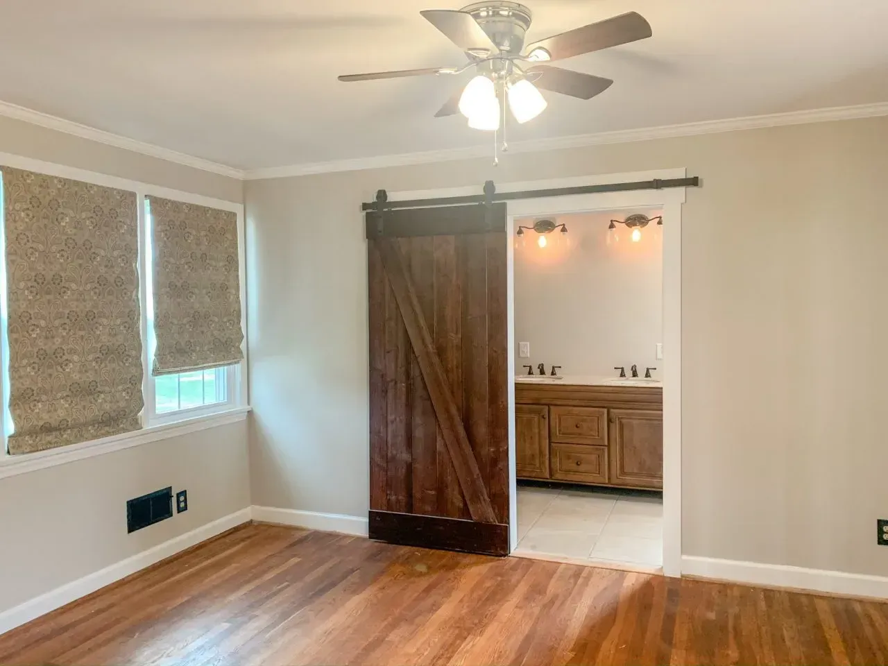 An empty room with a sliding barn door and a ceiling fan.