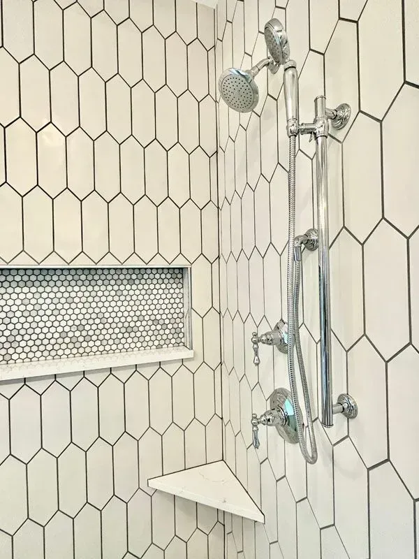 A bathroom with white tiles and a shower head.