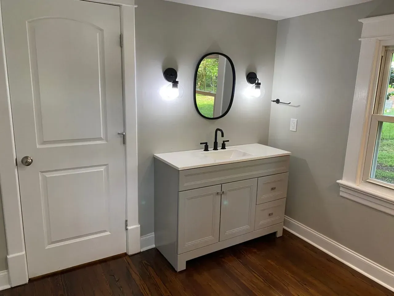 A bathroom with a sink , mirror and window.