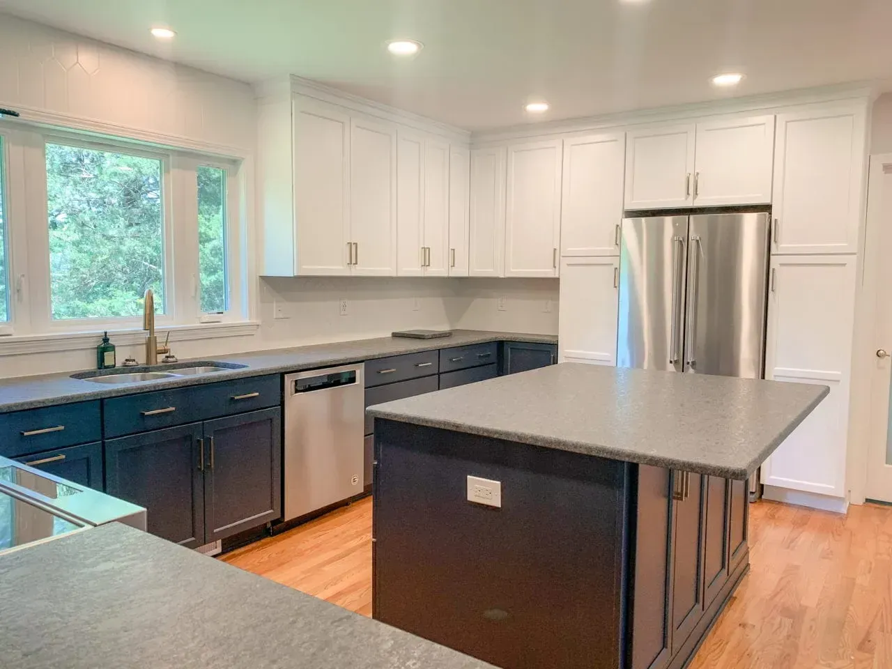 A kitchen with blue cabinets , stainless steel appliances , granite counter tops and a large island.