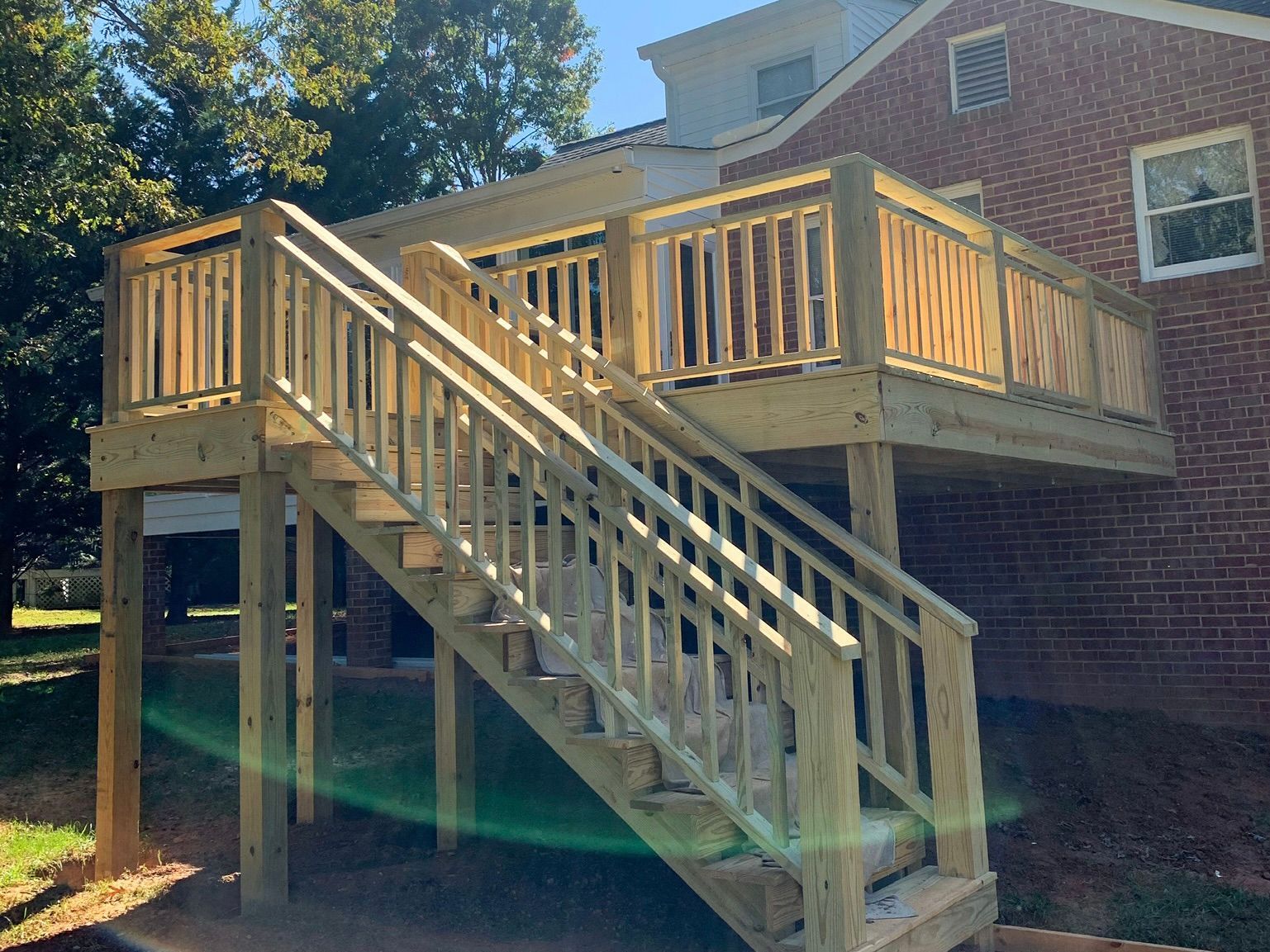 A wooden deck with stairs leading up to it is in front of a brick house.