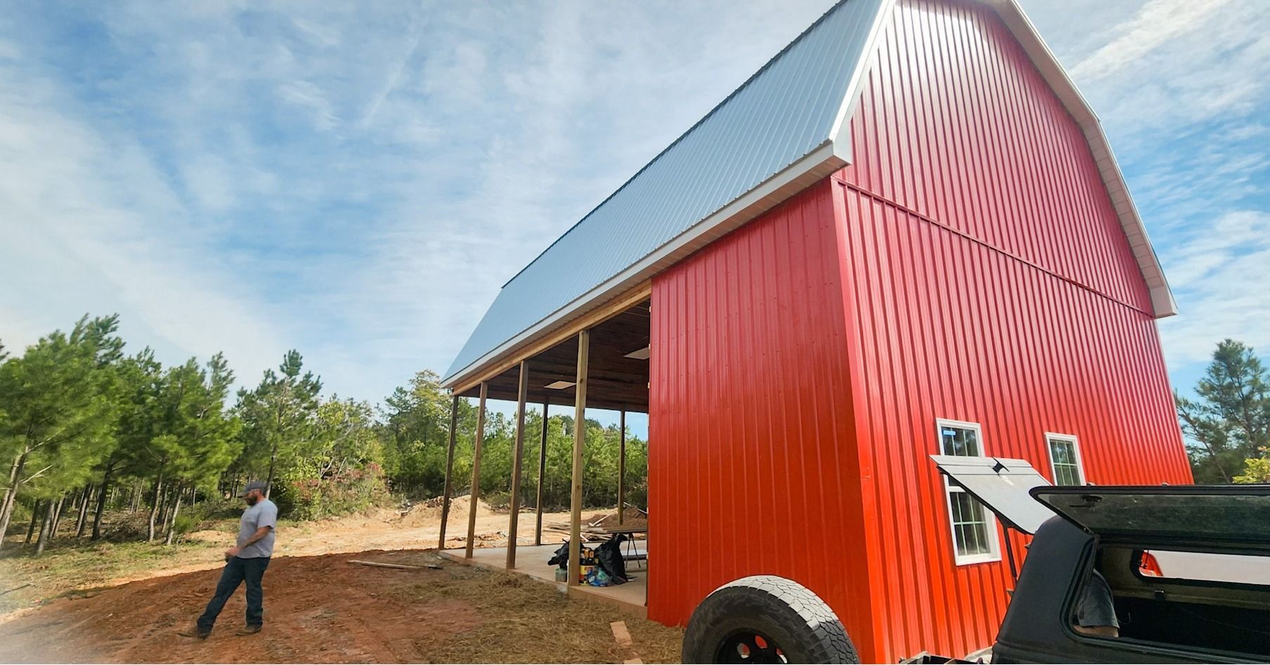 A man is standing in front of a large red barn.