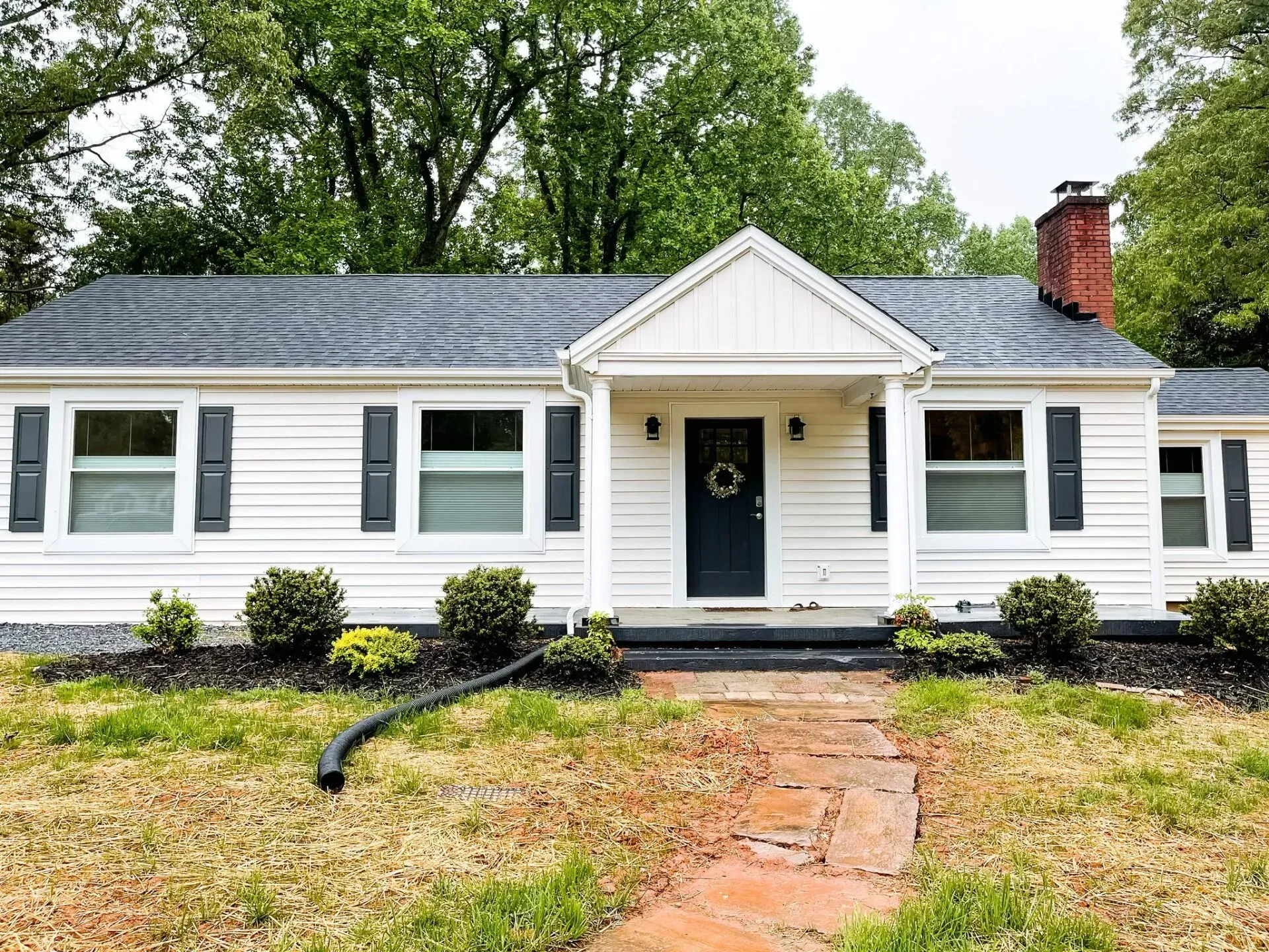 A white house with black shutters and a brick walkway in front of it.