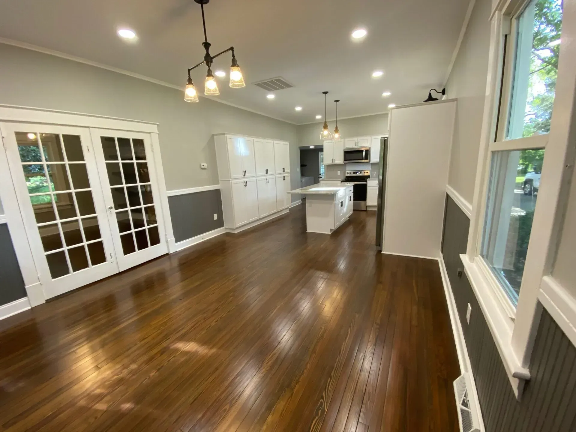 A living room with hardwood floors and a kitchen in the background.