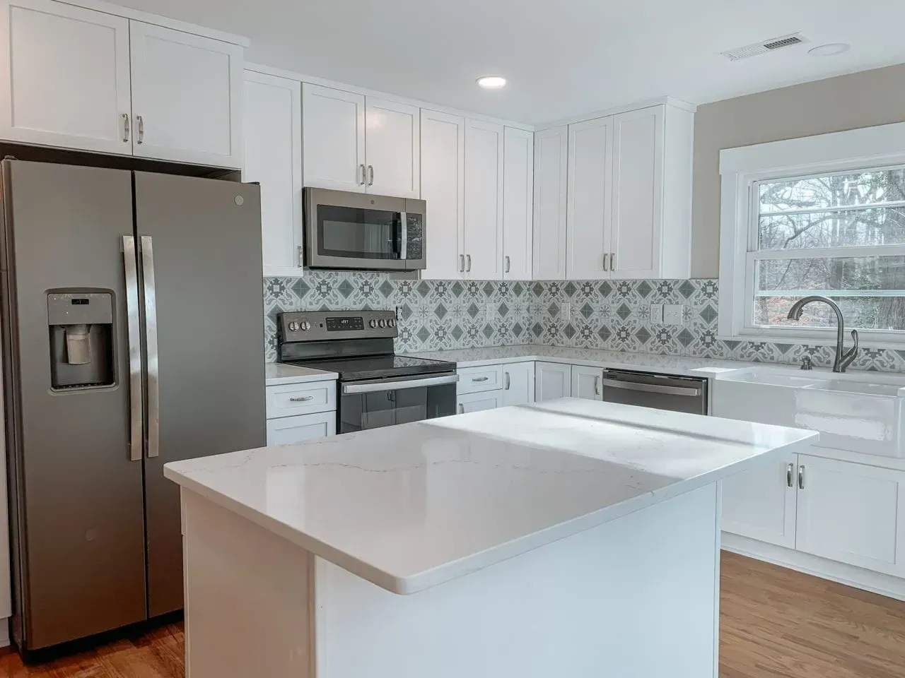 A kitchen with white cabinets , a stainless steel refrigerator , a microwave , and a sink.