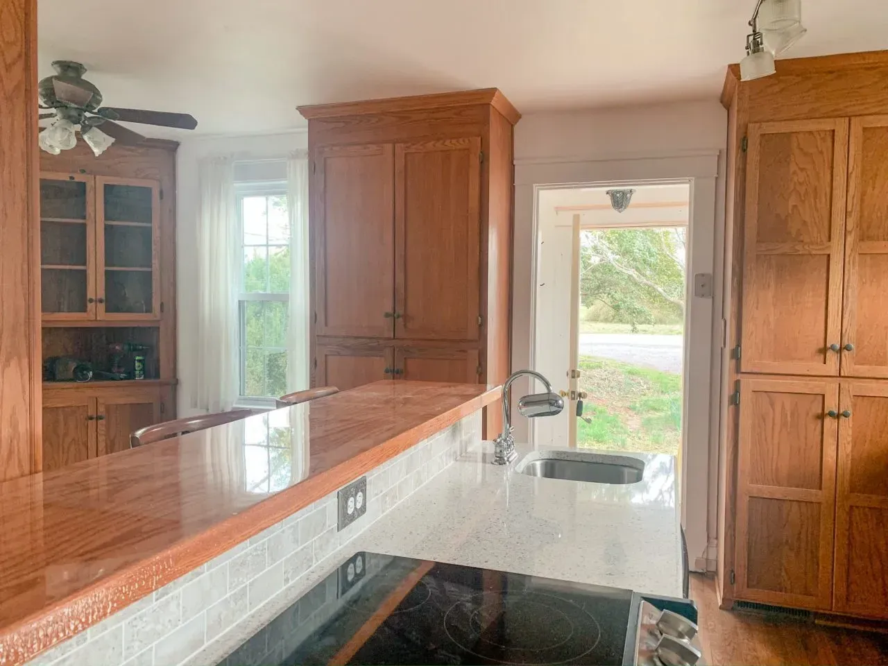 A kitchen with wooden cabinets , a stove , a sink , and a ceiling fan.