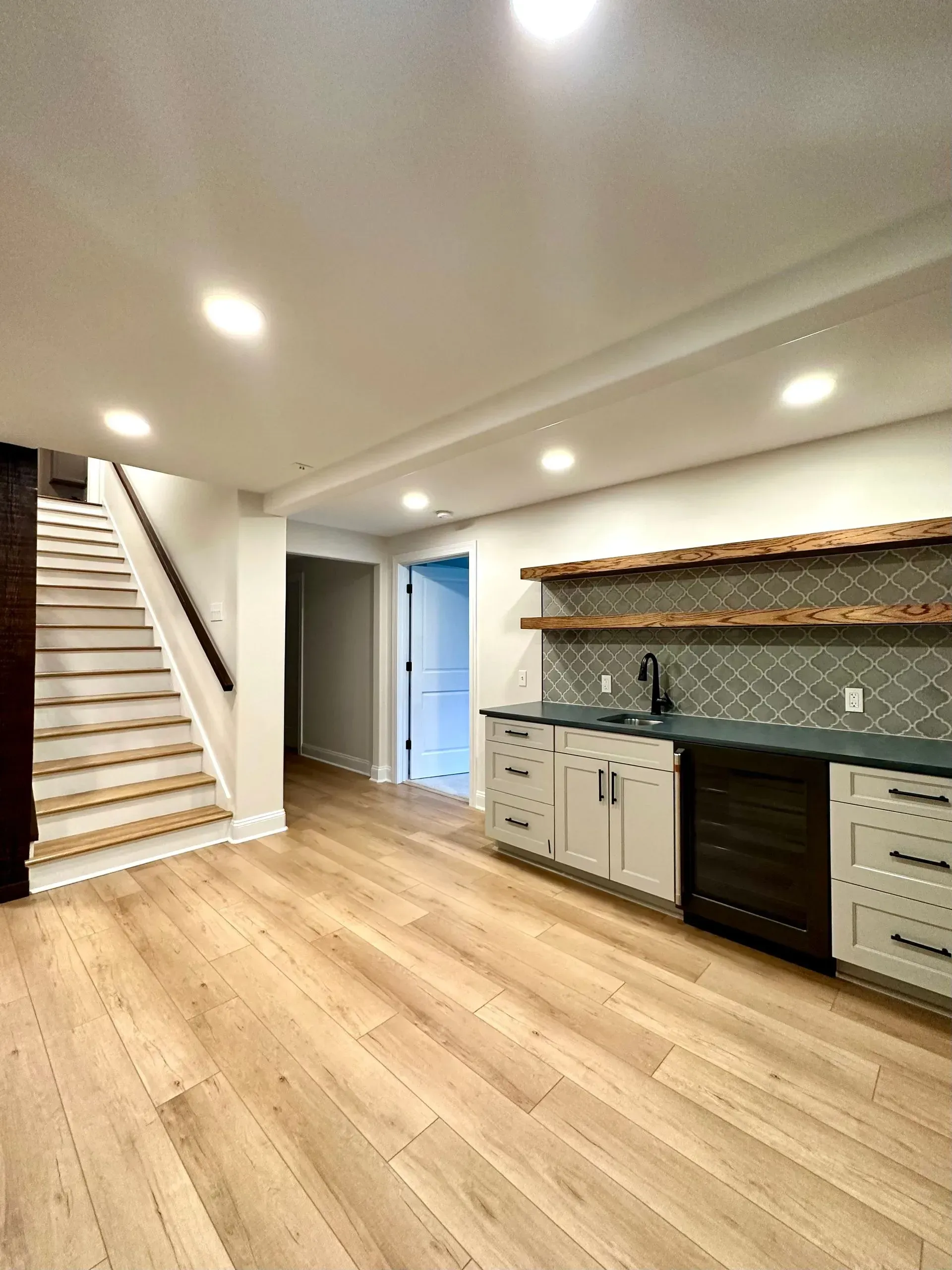 A kitchen in a basement with hardwood floors and stairs.