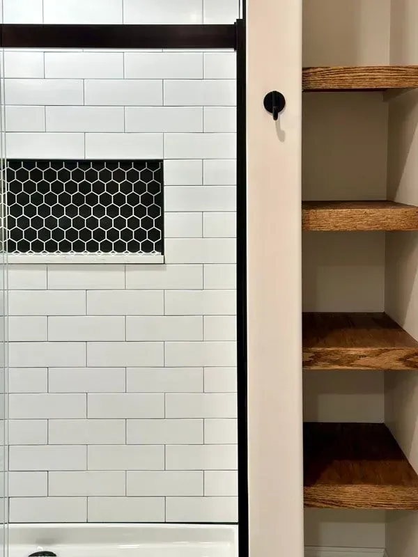 A bathroom with white subway tiles and wooden shelves.