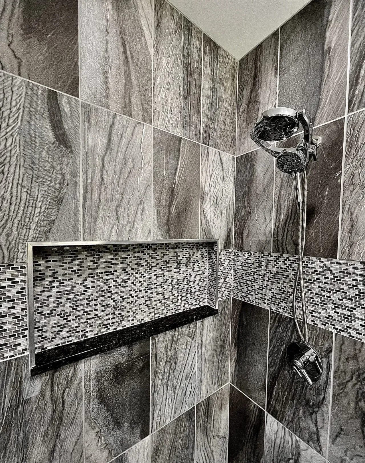 A black and white photo of a shower with a shower head and a shelf.