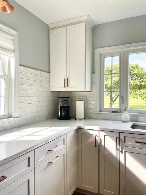 A kitchen with white cabinets , a sink , a coffee maker and a window.