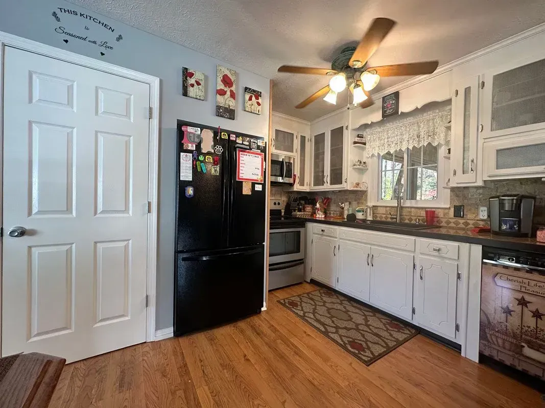 A kitchen with white cabinets , a black refrigerator and a ceiling fan.