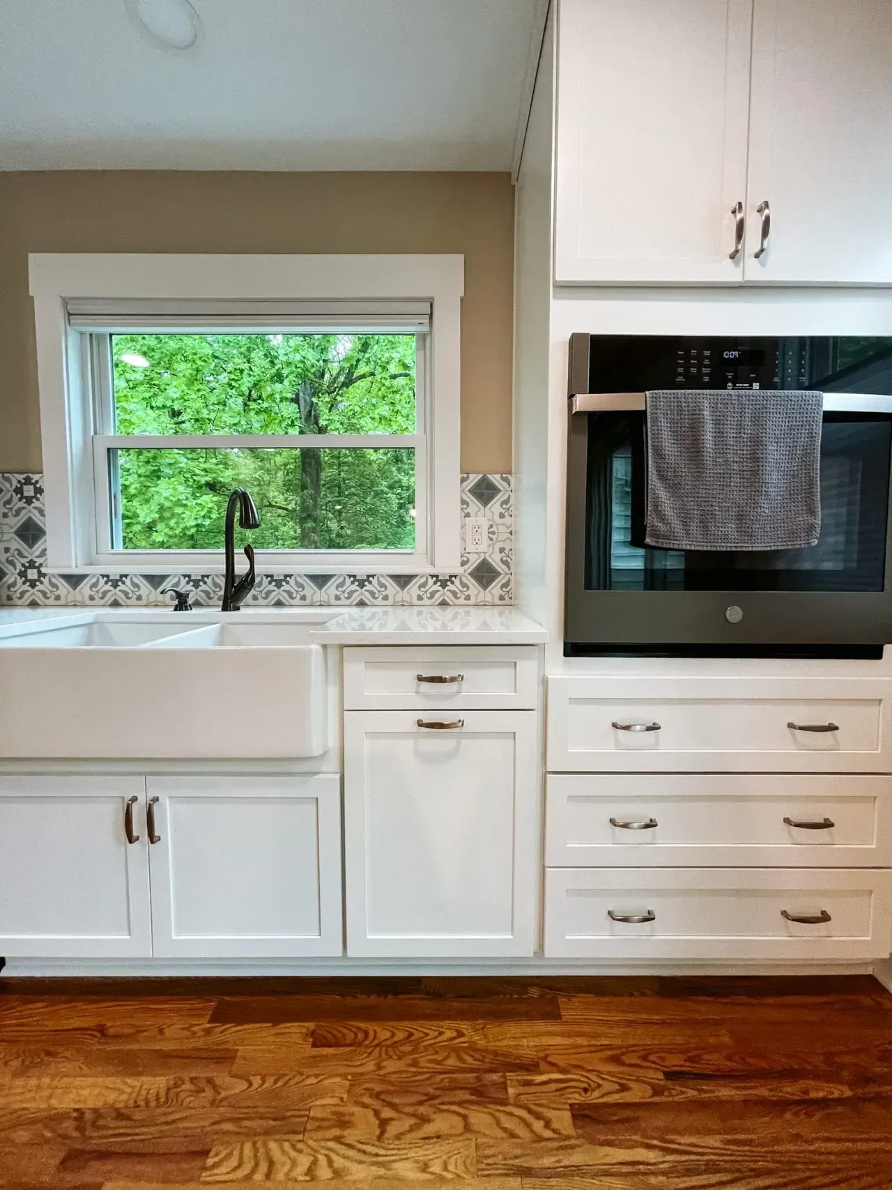 A kitchen with white cabinets , a sink , an oven , and a window.