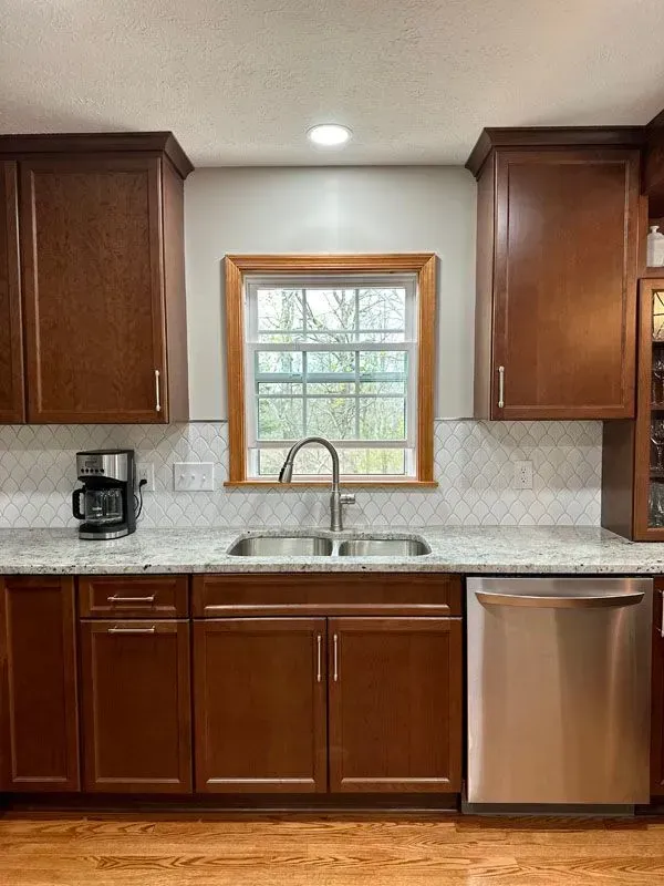 A kitchen with wooden cabinets , stainless steel appliances , a sink , and a window.