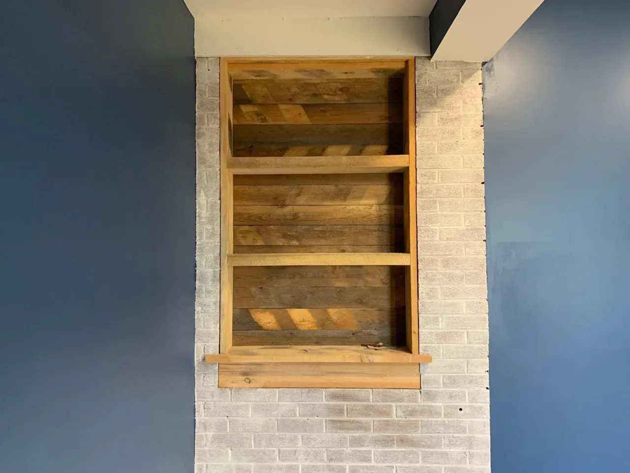 A wooden shelf is built into a brick wall.