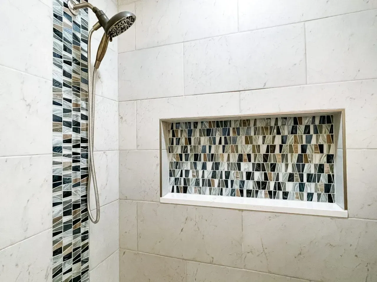A shower with a mosaic tile niche and a shower head.