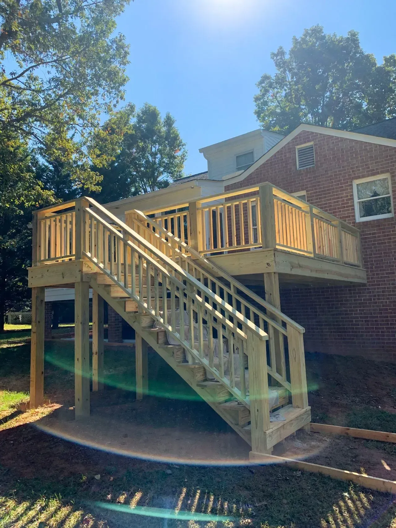 A wooden deck with stairs leading up to it is in front of a brick house.