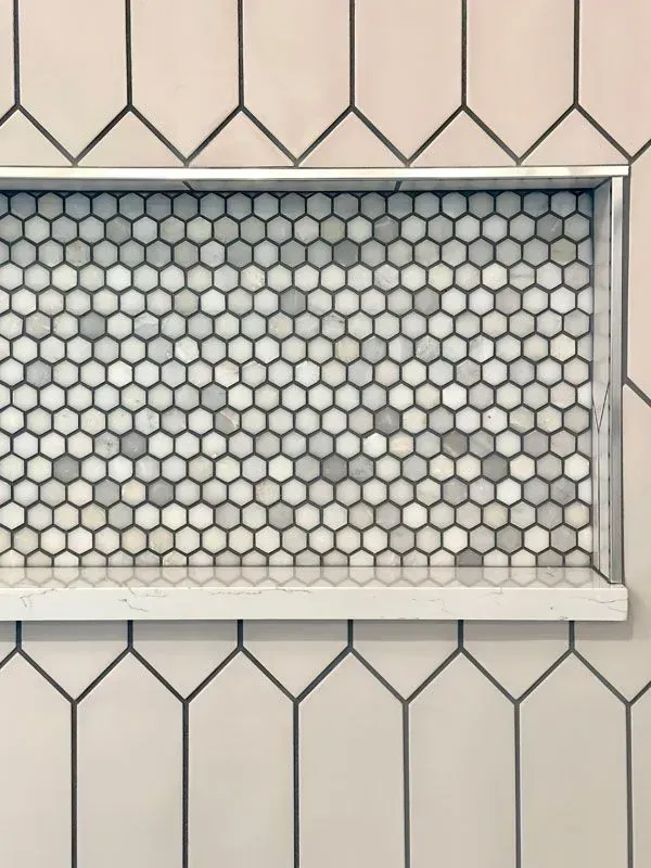 A close up of a shower niche with honeycomb tiles on a wall.