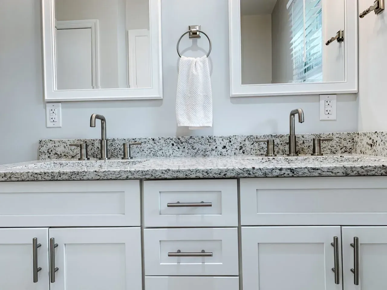 A bathroom with two sinks , two mirrors , and white cabinets.