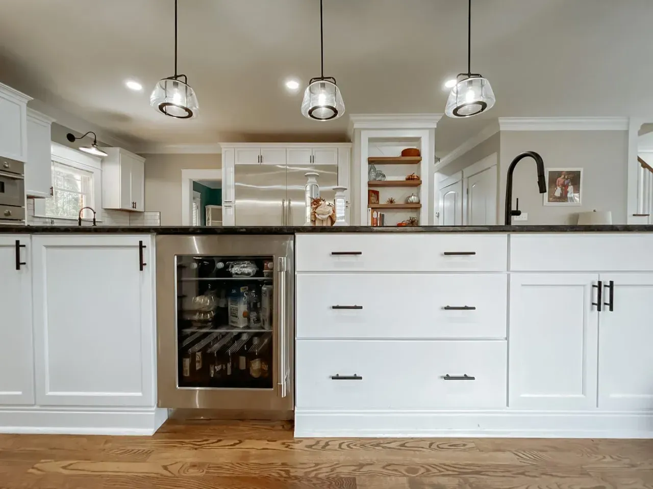 A kitchen with white cabinets , stainless steel appliances , a refrigerator and a wine cooler.