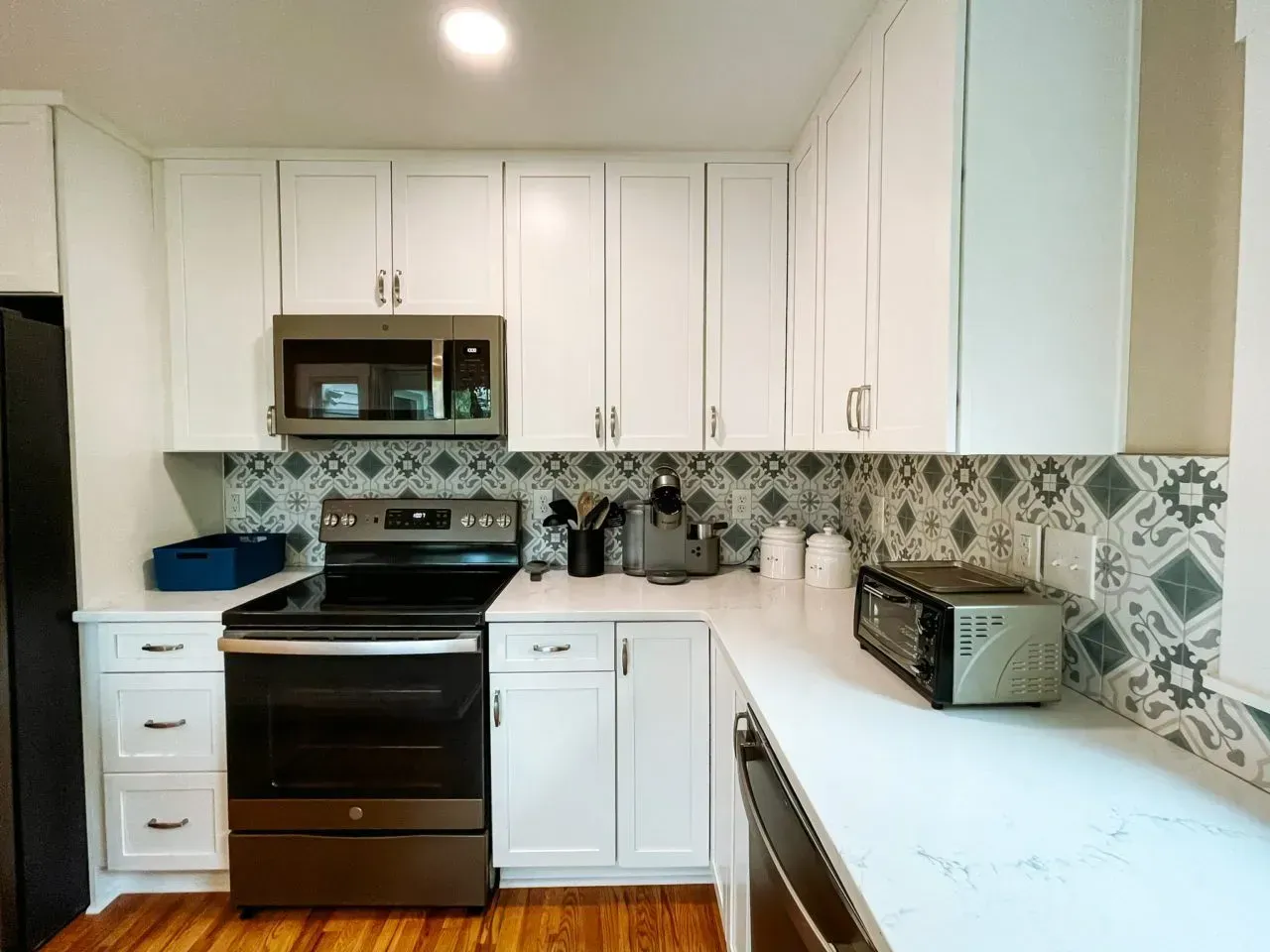 A kitchen with white cabinets , a stove , a microwave , and a refrigerator.