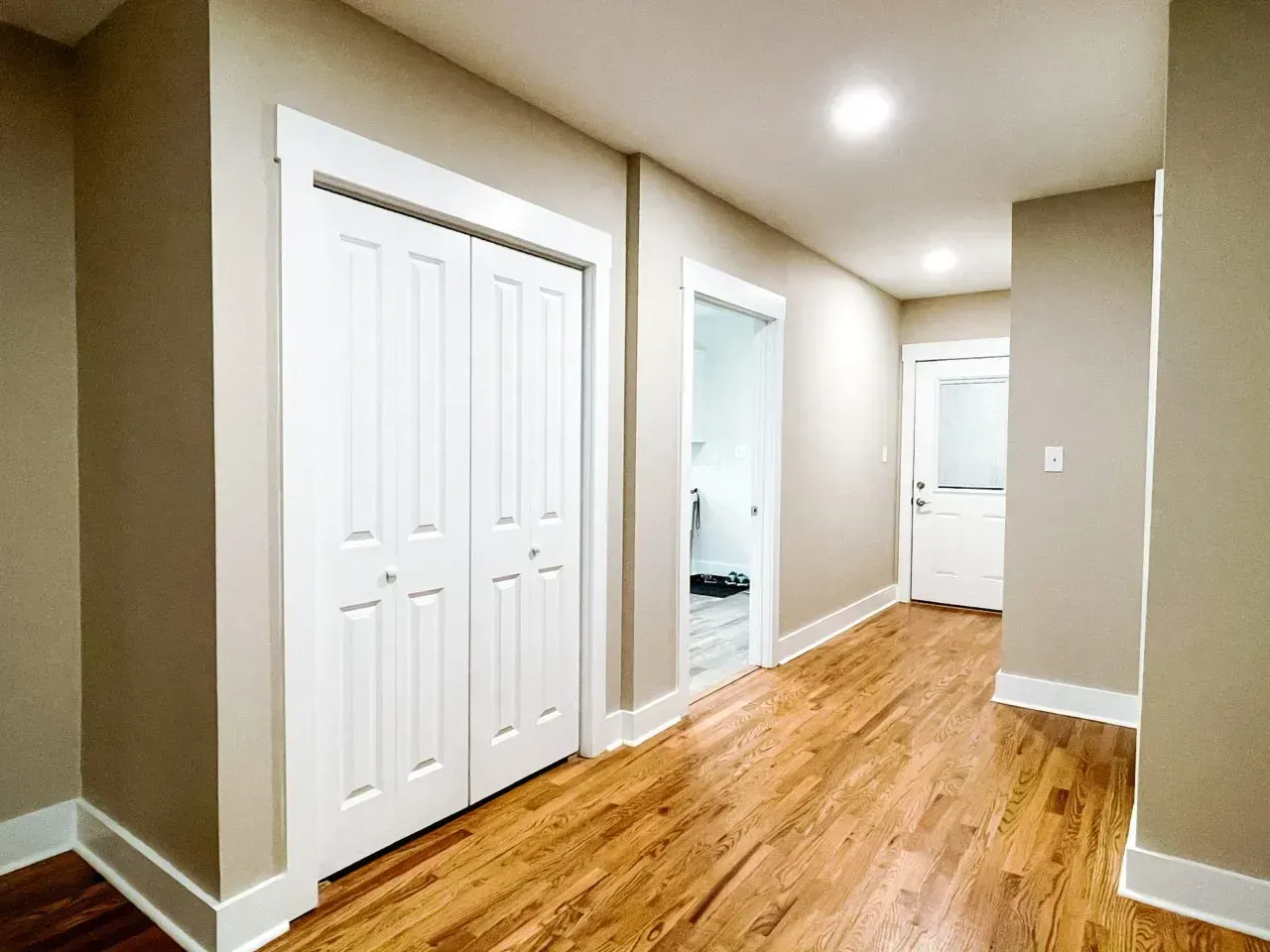 A hallway with hardwood floors and white doors leading to a bathroom.