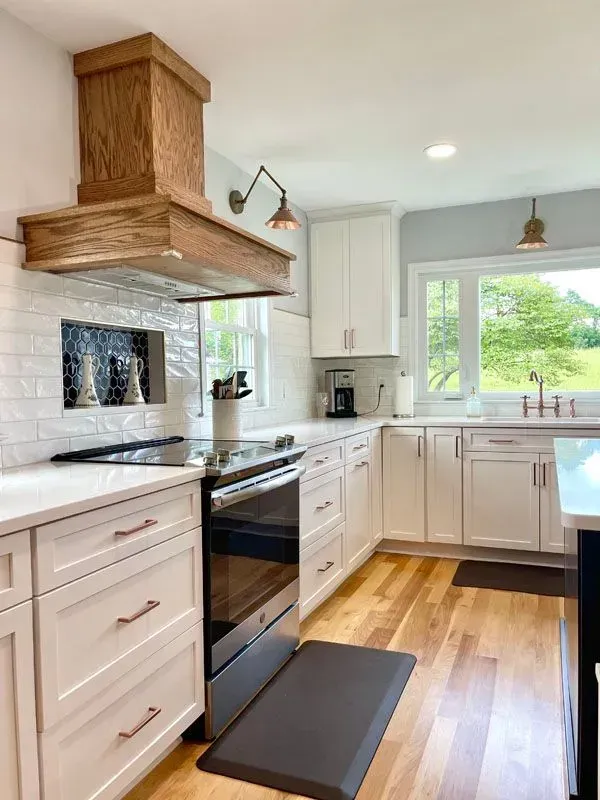 A kitchen with white cabinets , stainless steel appliances , hardwood floors and a wooden hood.