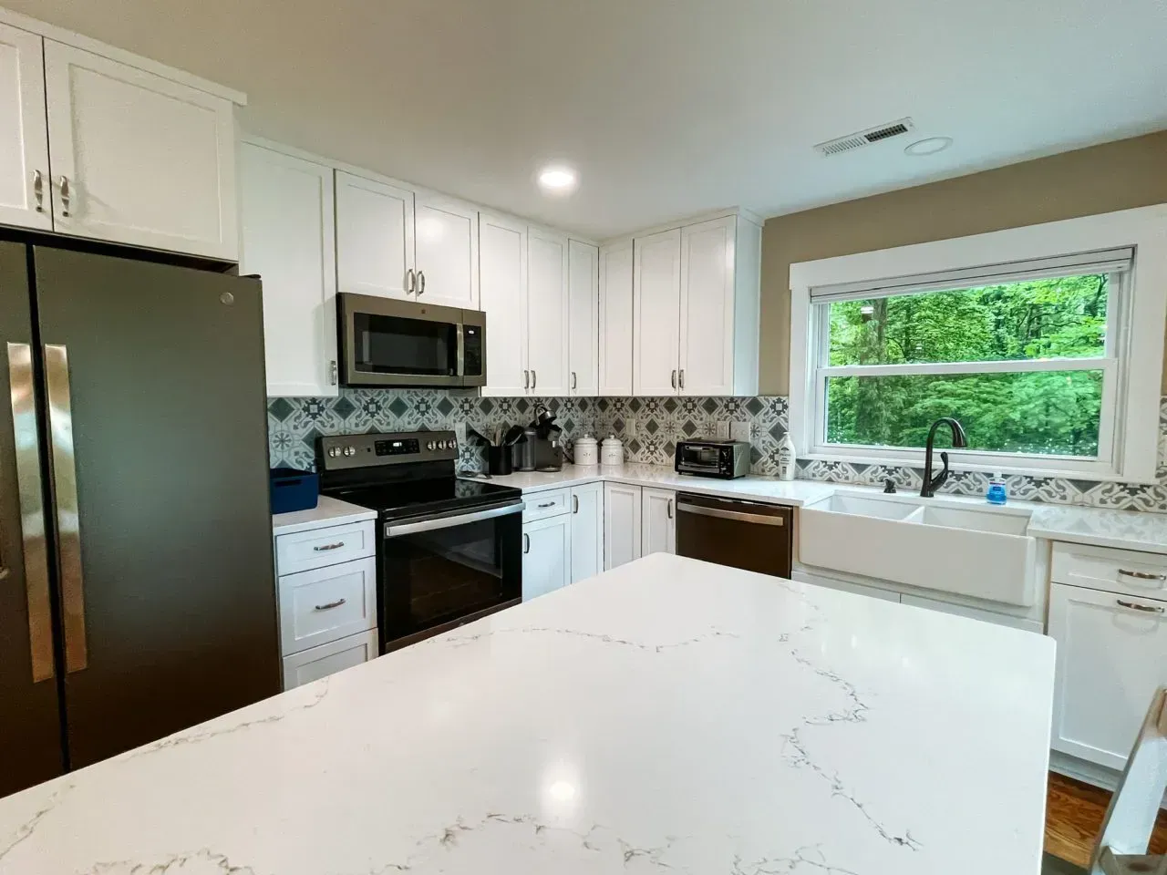 A kitchen with white cabinets , stainless steel appliances , and a large island.
