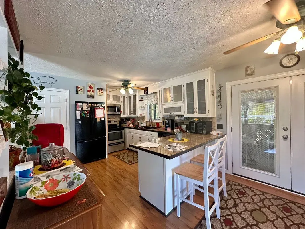 A kitchen with a ceiling fan , stools , a refrigerator , and a table.