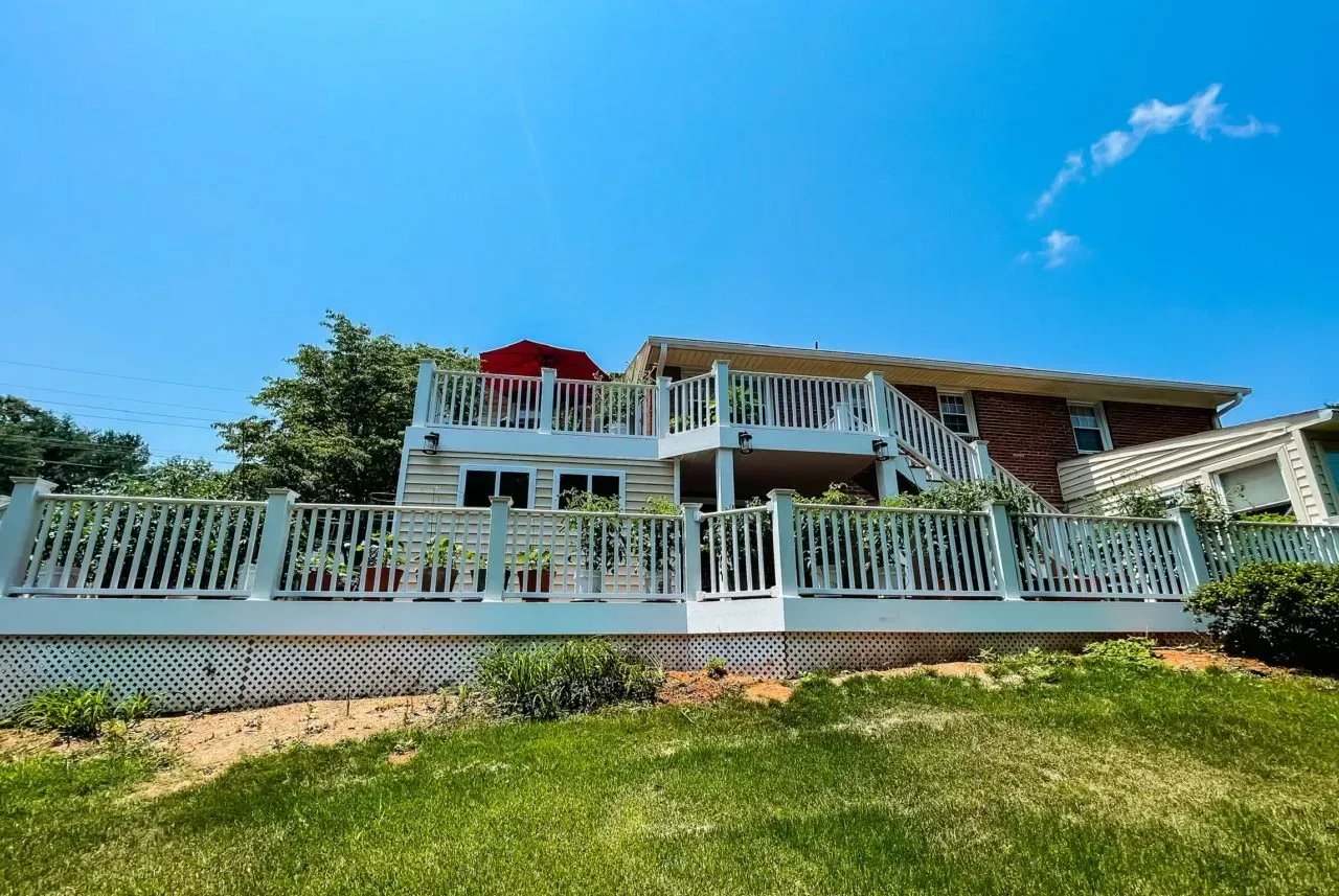 A large house with a large deck on top of it is sitting on top of a lush green hillside.