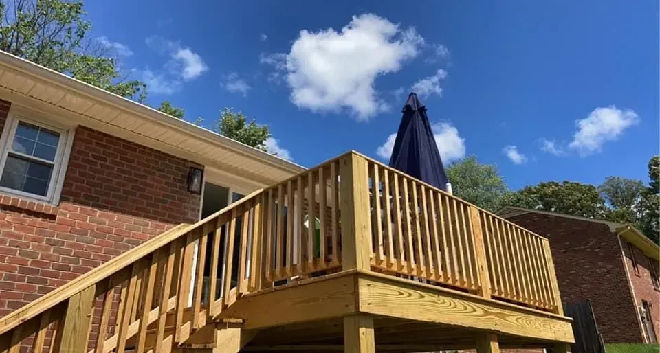 A wooden deck with stairs and an umbrella in front of a brick house.