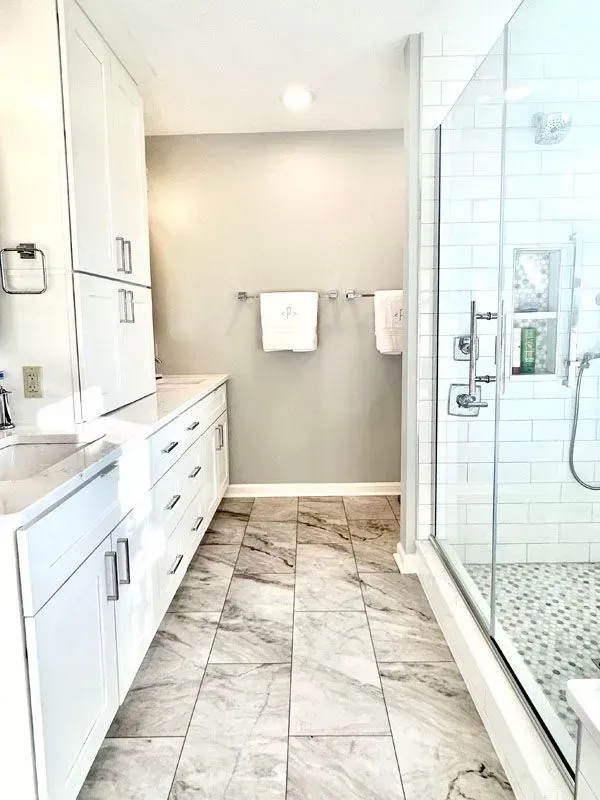 A bathroom with a walk in shower , sink , and cabinets.