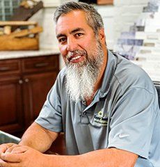 A man with a beard is sitting at a desk in a kitchen.