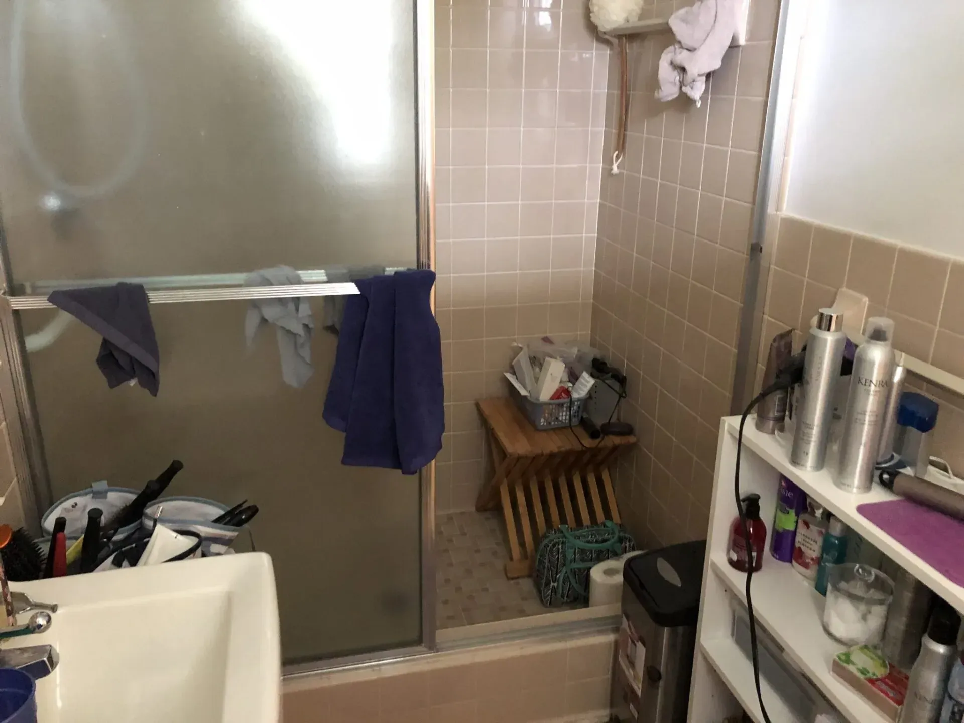 A bathroom with a sink , shower , and a stool.