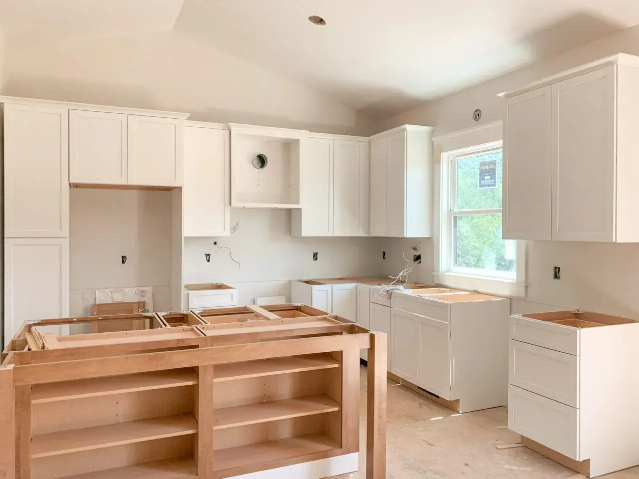 A kitchen under construction with white cabinets and wooden shelves.
