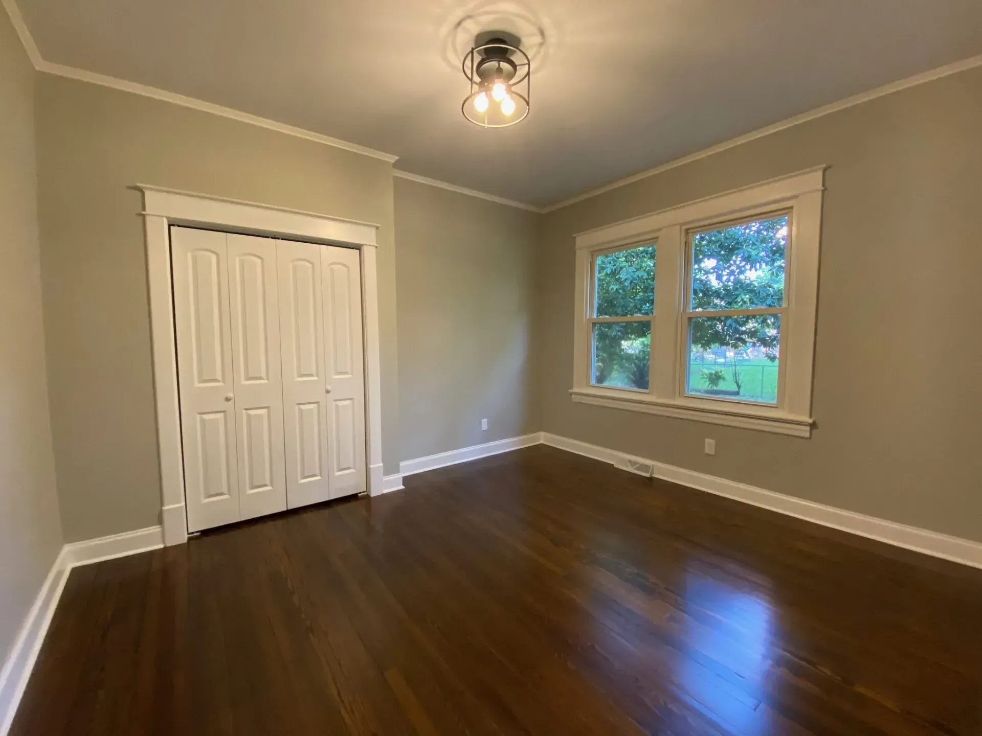 An empty room with hardwood floors and two windows.