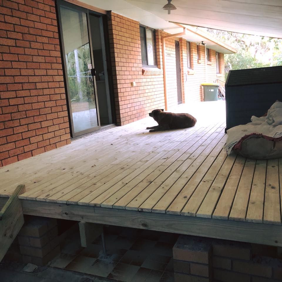 Brown Dog Resting on a Wooden Deck Next to a Brick Building — Alcando Renovations and Maintenance In Forster, NSW