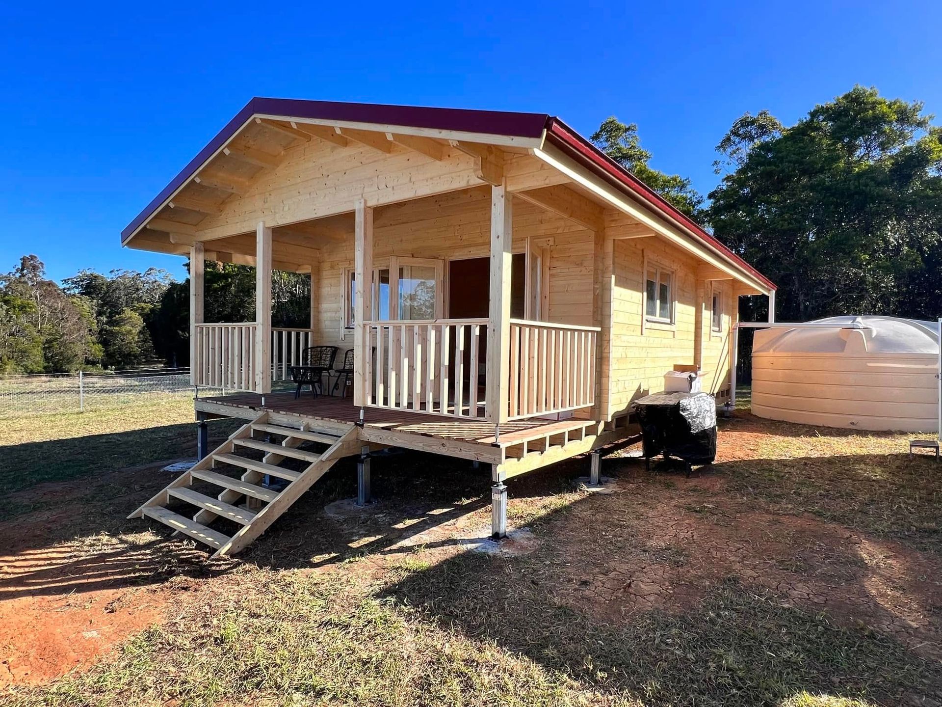 Wooden Cabin With Red Roof and Porch, Set on a Grassy Hill — Alcando Renovations and Maintenance In Old Bar, NSW